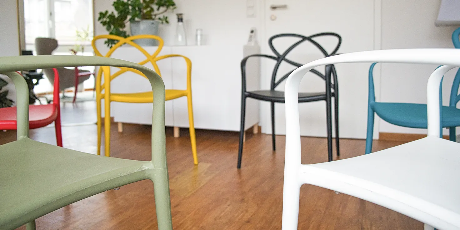 Drei moderne, graue Stühle im Kreis angeordnet für eine Gruppentherapie-Sitzung in einem hellen, einladenden Raum.