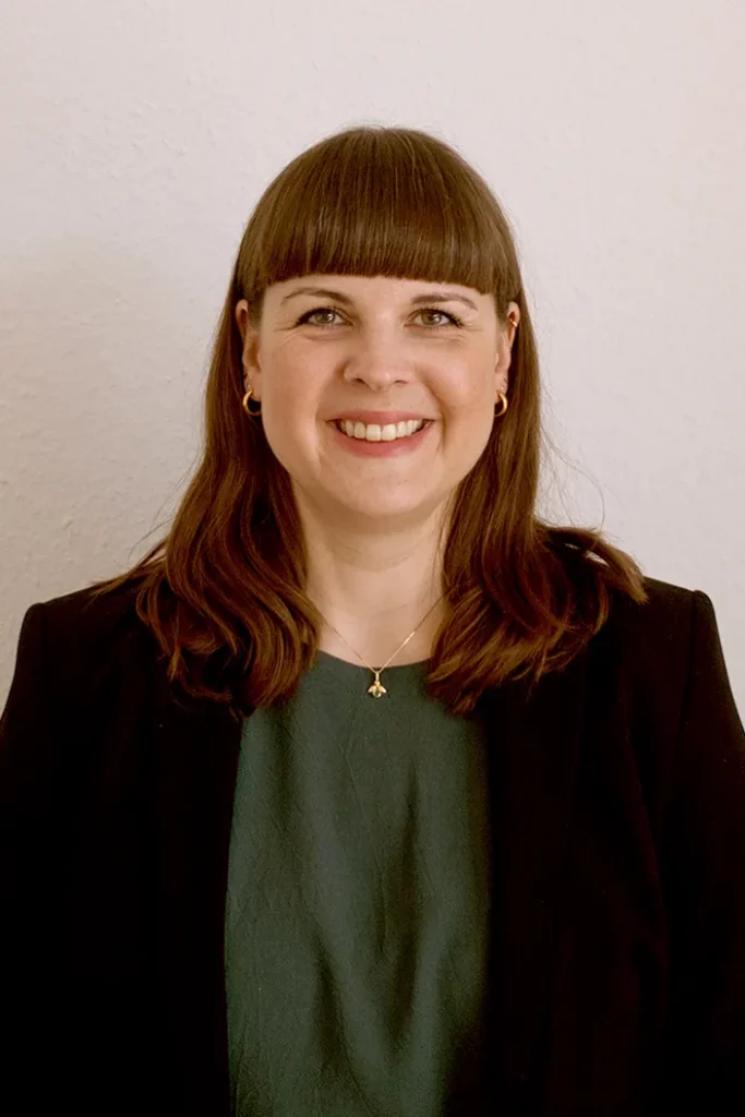 Porträt von Stella Heimsch, Psychotherapeutin, lächelnd vor einer weißen Wand.