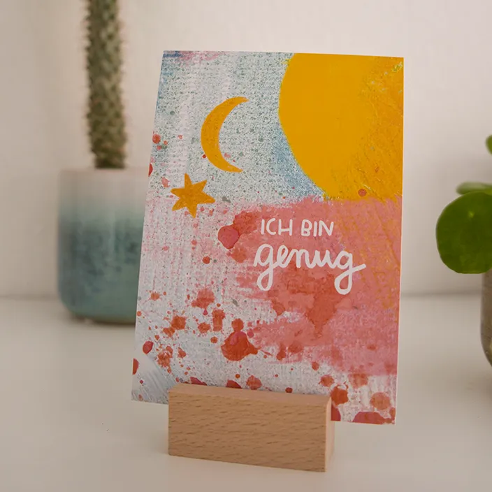 Eine dekorative Karte mit einem inspirierenden Zitat auf einem hölzernen Schreibtisch, umgeben von einem Bleistift und einem kleinen grünen Notizblock.